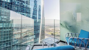 Un balcon doté d’une balustrade en verre, d’un fauteuil bleu rembourré et d’une petite table.