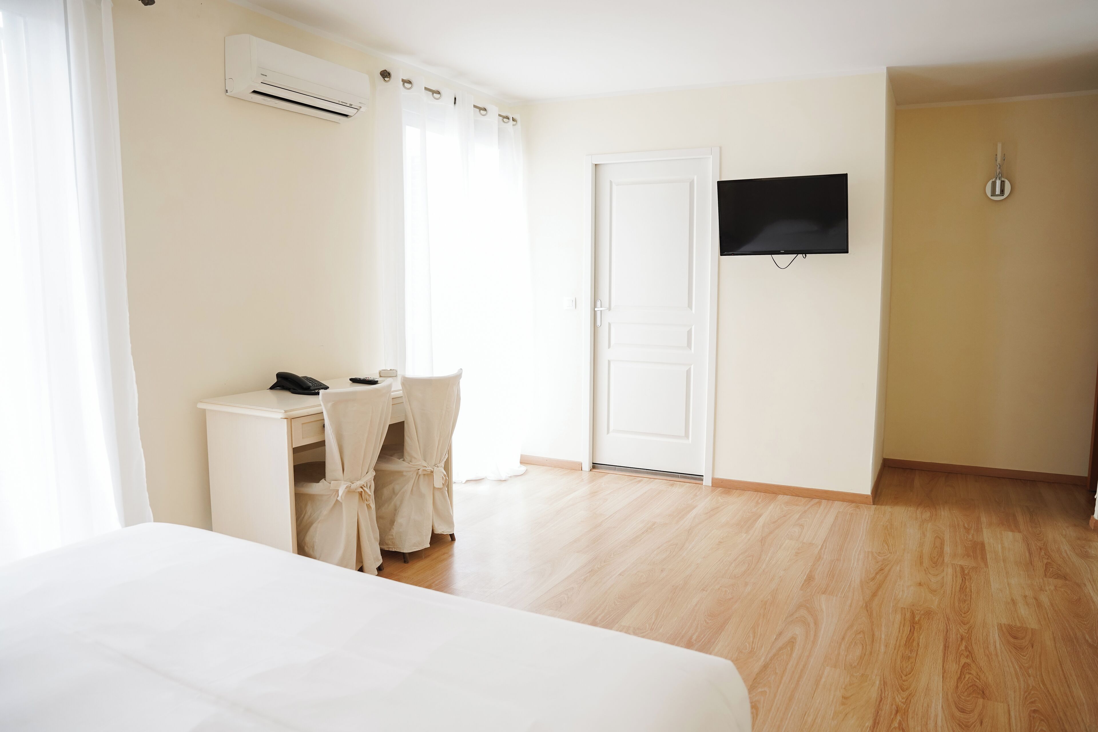Una habitación de hotel con cama, escritorio con silla, televisor y aire acondicionado.