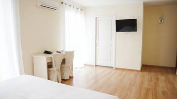 Una habitación de hotel con cama, escritorio con silla, televisor y aire acondicionado.