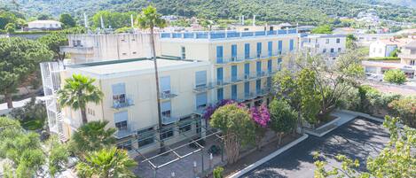 A multi-story hotel with balconies, surrounded by greenery and mountains.