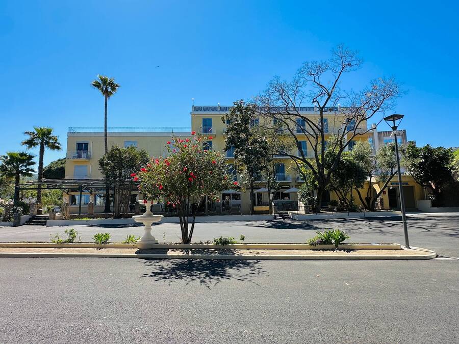 A hotel with a yellow facade, multiple balconies, and a central courtyard with a fountain and trees.