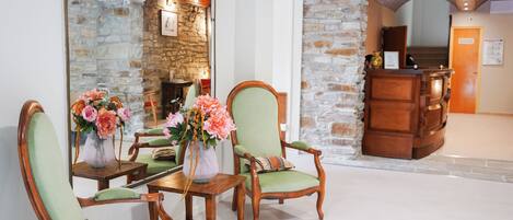 A lobby with a stone wall, a reception desk, and green upholstered chairs.