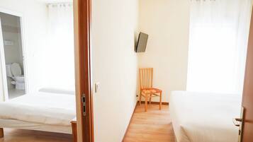 Ein Hotelzimmer mit zwei Betten, einem Holzstuhl, einem an der Wand befestigten Fernseher und Holzboden.