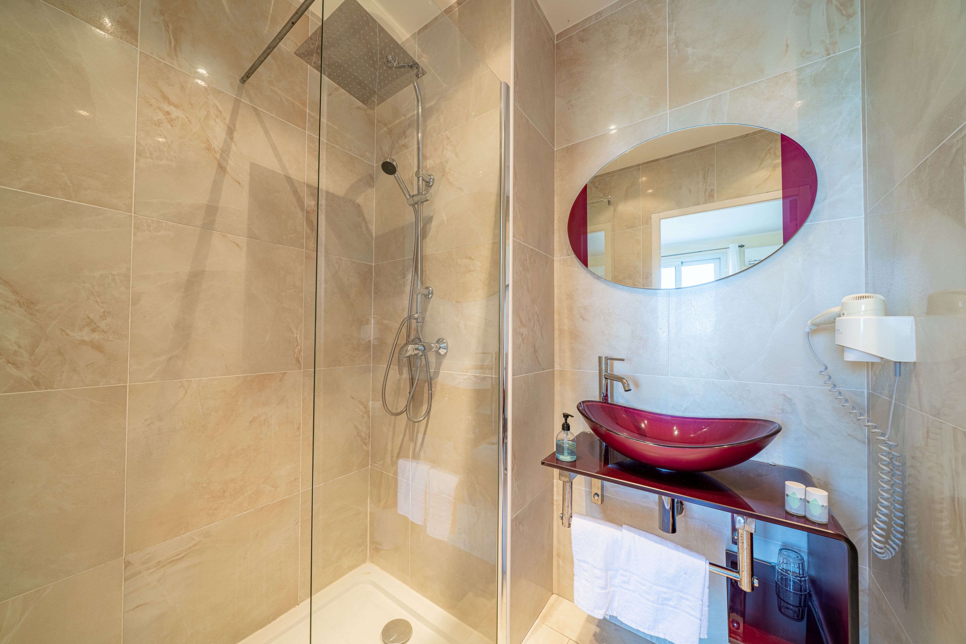 Un bagno moderno con doccia a vetro, lavabo a colonna rosso e specchio con cornice rossa.