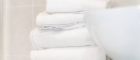 A stack of white towels in a bathroom with a tiled wall in the background.