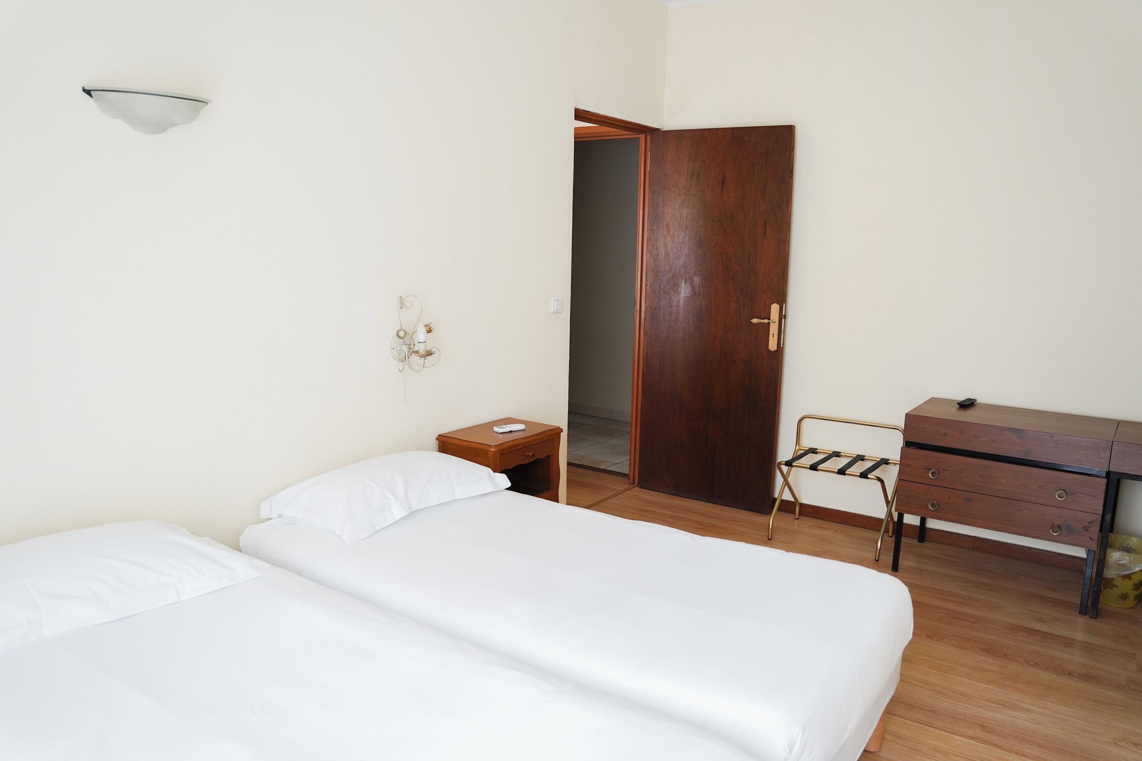 A bedroom with two beds, a wooden dresser, a nightstand, and a door leading to another room.