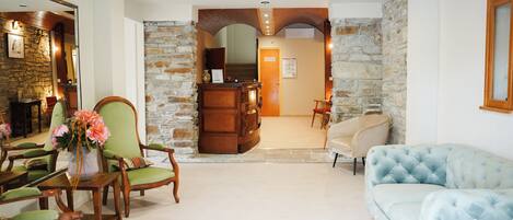 A lobby with a stone wall, wooden reception desk, green upholstered chairs, and a light blue tufted sofa.