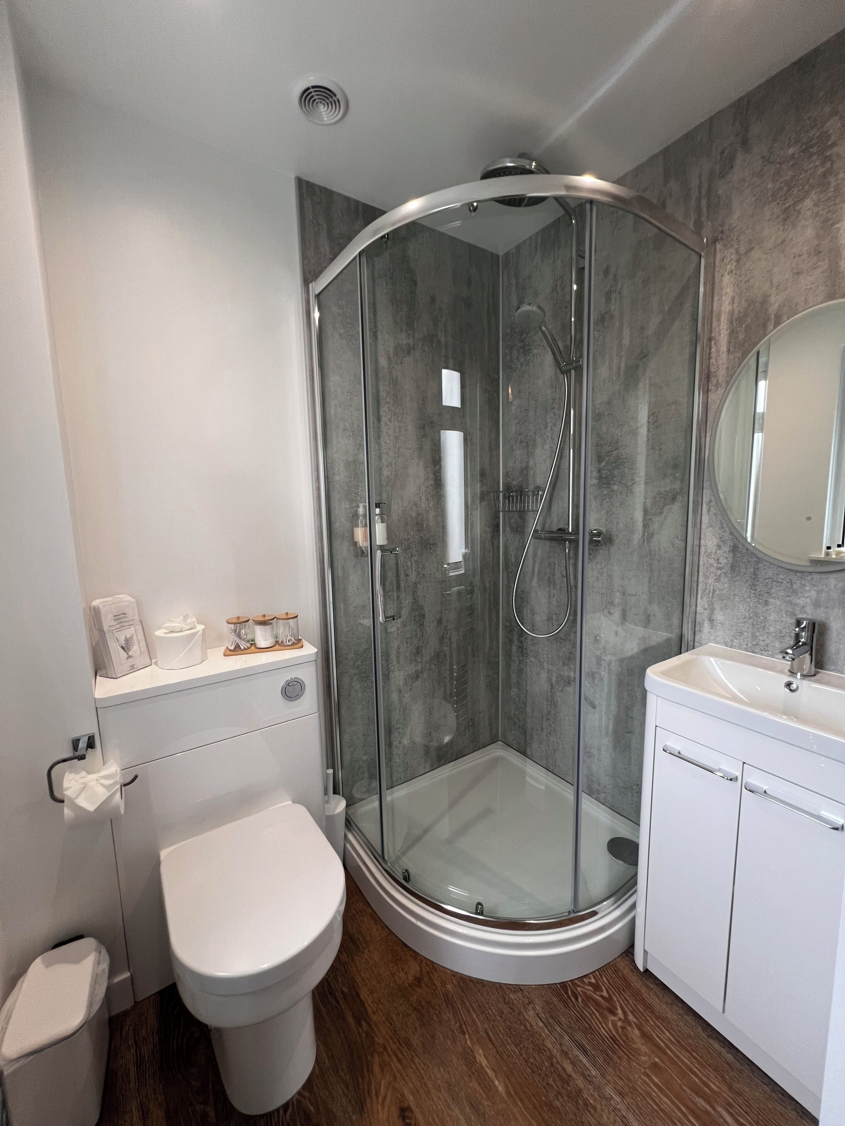 Un baño moderno con cabina de ducha de vidrio, inodoro y lavamanos con espejo sobre él.