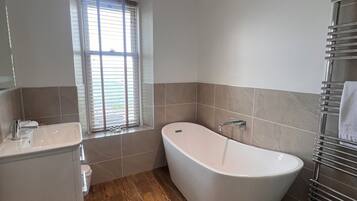 A modern bathroom with a freestanding bathtub, a window with blinds, a toilet, and a sink.