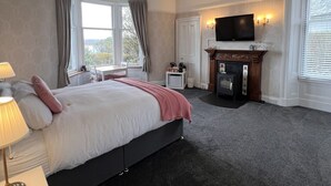 A hotel room with a bed, a TV, a fireplace, and a window.