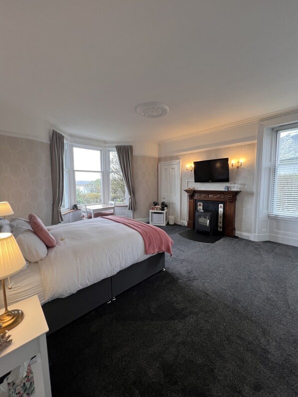 A hotel room with a bed, a TV, a fireplace, and a window. - Ronebhal B&B (Oban)