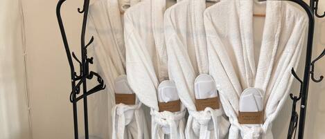 A hotel room with a black metal rack holding white robes and towels, a black suitcase, and a television mounted on the wall.