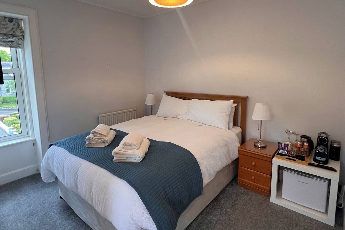 A neatly made bed with a blue blanket, a bedside table with a lamp, and a small cabinet.