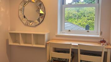 A room with a desk, two chairs, a window with a view of greenery, a wall-mounted mirror, and a 'NO SMOKING' sign.