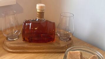 A wooden table with a bottle of amber-colored liquor, two empty glasses, and a small glass jar with a brown substance.