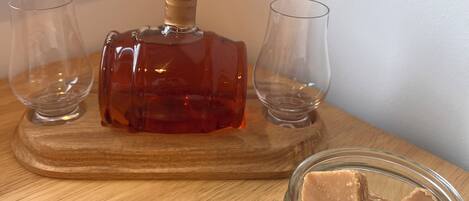 A wooden table with a bottle of amber-colored liquor, two empty glasses, and a small glass jar with a brown substance.