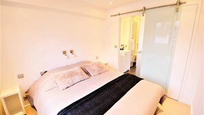 A modern bedroom with a large bed, a bedside table, and a sliding glass door leading to a bathroom.