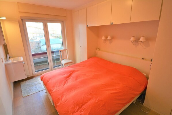 A bedroom with a bed, a sliding glass door, a chair, and a small table.
