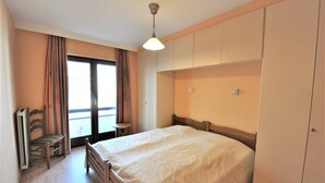 Um quarto com cama, uma cadeira, uma mesa pequena e um guarda-roupa.