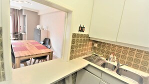 Cozinha compacta com mesa de madeira, duas cadeiras, pia e azulejos de revestimento estampados.