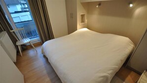 A bedroom with a large bed, a chair, and a window with curtains. - Apartment in Duinbergen with Side Sea View (KNOKKE-HEIST)