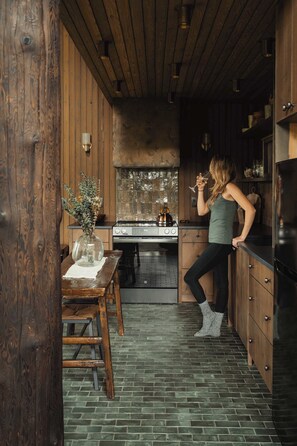 A kitchen with wooden walls, a stove, and a person holding a glass.