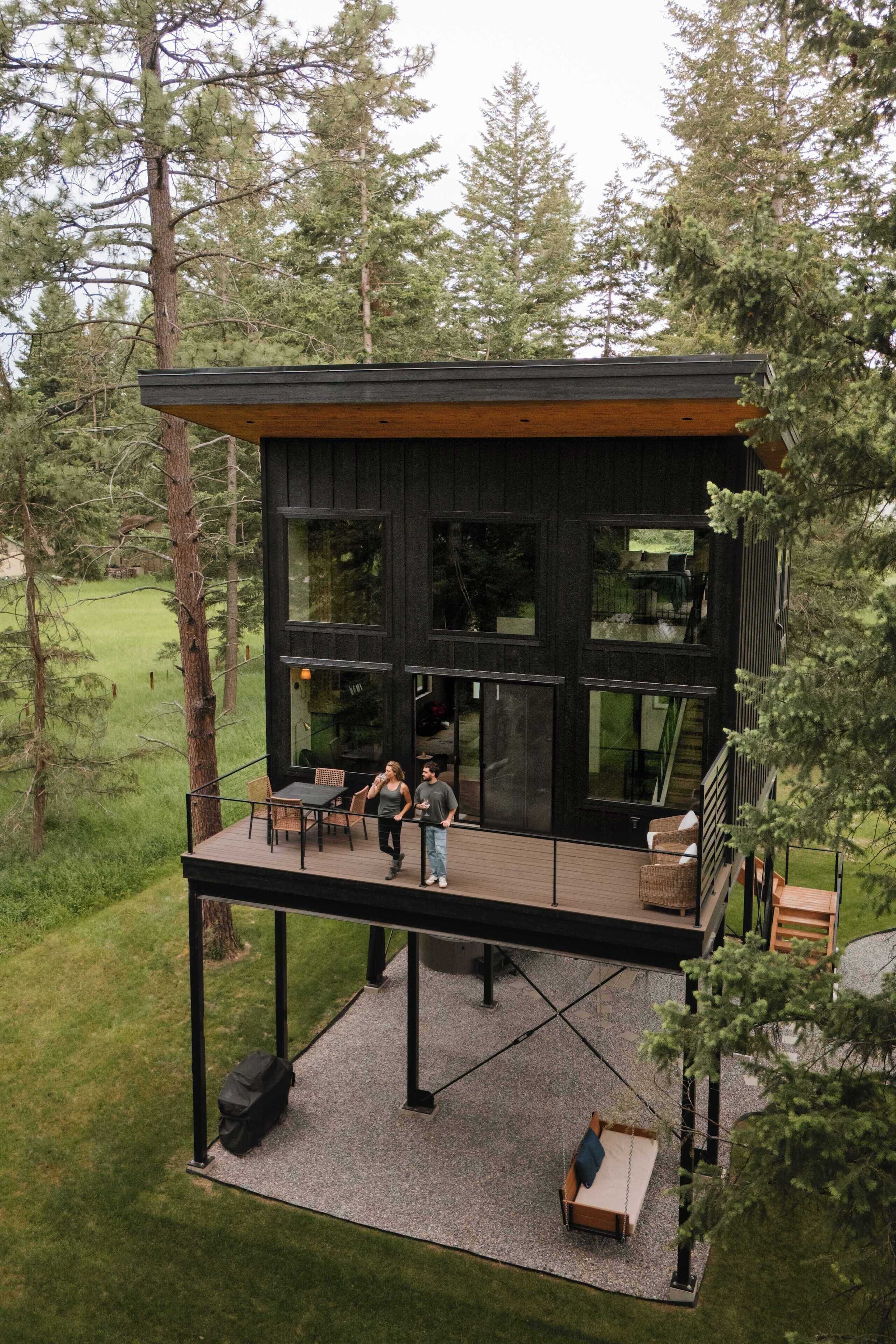 A modern cabin with a deck, large windows, and a staircase leading to an upper level.
