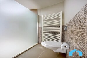 Une salle de bain moderne avec des toilettes, une douche à l’italienne et un mur recouvert de carreaux.