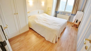 A bedroom with a bed, a radiator, a window with curtains, and a door with a handle.