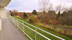 A balcony with a white railing overlooking a grassy area with trees and a path.