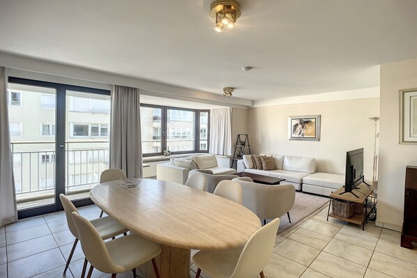 A modern living room with a dining table, sofas, and a TV.