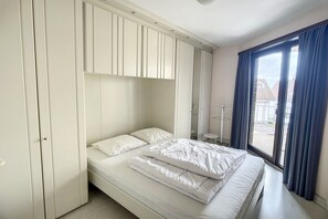 Um quarto com cama, guarda-roupa, uma mesinha e janela com cortinas.
