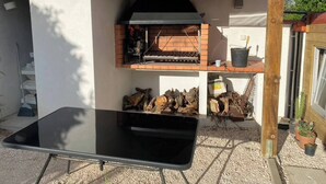 Une cuisine extérieure équipée d’un barbecue, d’une table et d’un espace pour entreposer du bois de chauffage.