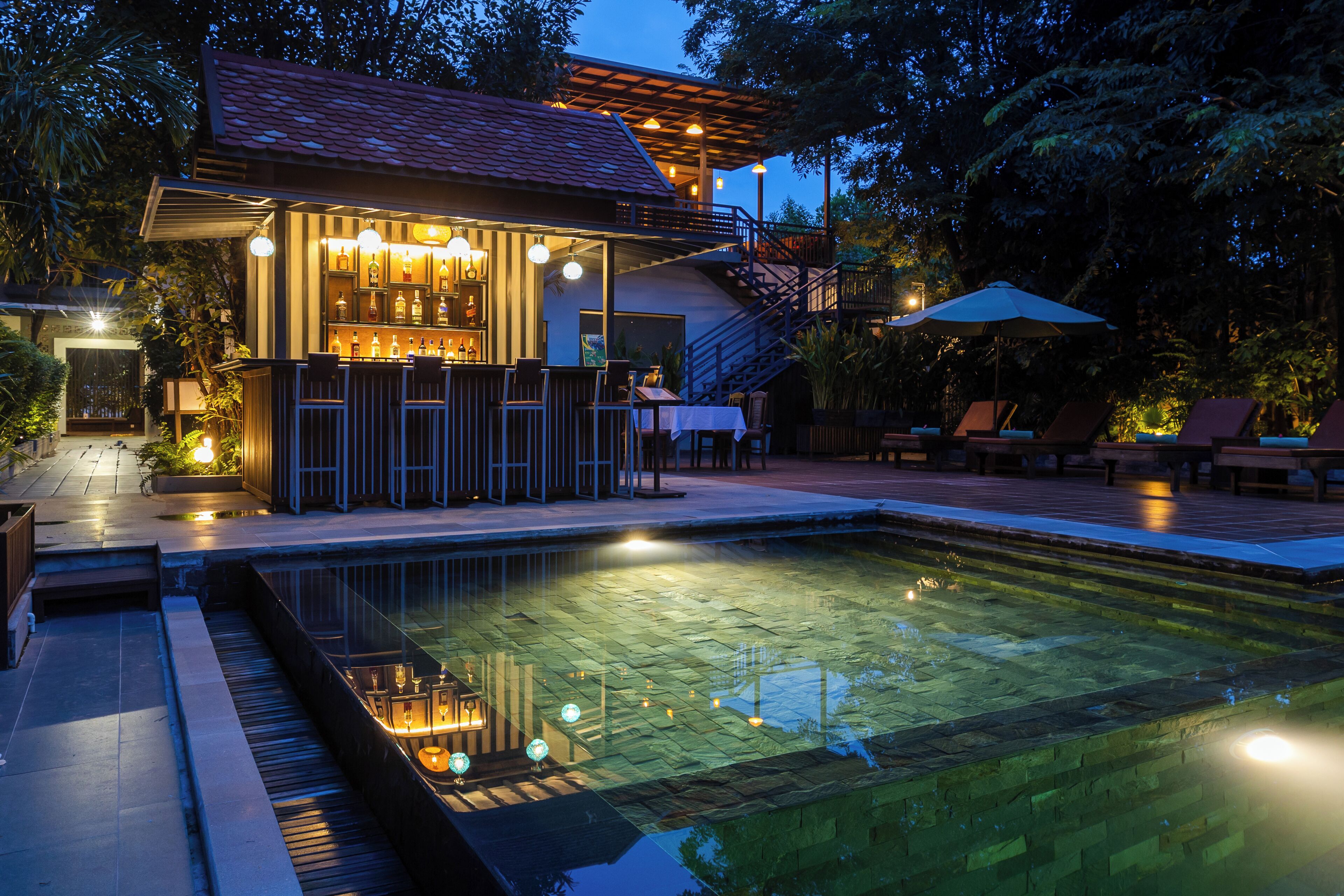 Uma área de bar à beira da piscina, com assentos e uma escadaria para um andar superior.