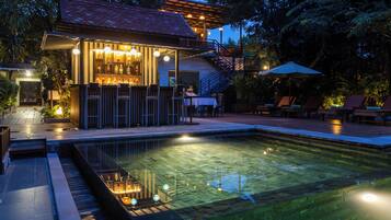 Uma área de bar à beira da piscina, com assentos e uma escadaria para um andar superior.