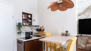 Een compacte keuken met een marmeren achterwand, een koffieapparaat, en een klein eethoekje met een televisie en een decoratieve plant.