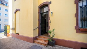 A yellow building with a black door, a small set of steps, and a potted plant.