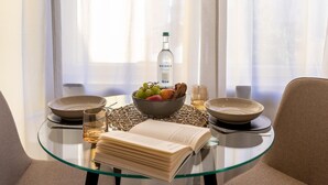 A dining table with a bowl of fruit, a bottle of Rhodius, and a book.