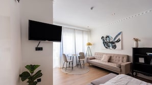 A modern living room with a flat-screen TV, a round dining table with chairs, a sofa, and a large abstract painting.