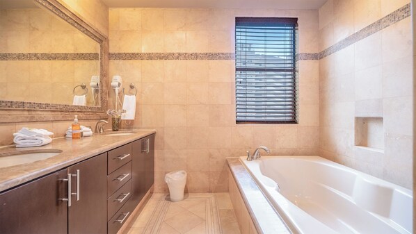 Un baño moderno con dos lavamanos, una bañera grande y una ventana con persianas.