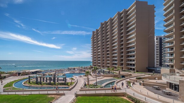 Un hôtel de grande hauteur doté de nombreux balcons, d’un espace piscine agrémenté d’une fontaine centrale et offrant une vue sur l’océan.