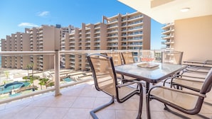 Ein Balkon mit Glastisch und Stühlen, mit Blick auf einen Pool und hohe Gebäude.