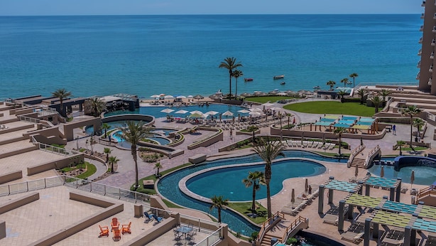 Ein Resort mit mehreren Swimmingpools, Palmen und Blick auf den Ozean.