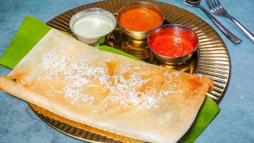 A dosa with three chutneys and a small bowl of liquid on a plate.