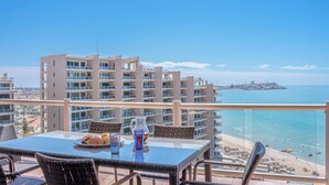 Ein Balkon mit Glastisch, Korbstühlen und Blick auf Strand und Meer.