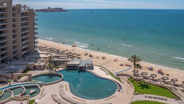 Ein Resort mit großzügiger Poolanlage, einem Strand und Blick auf den Ozean.