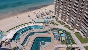 A resort with a large pool area, a beach, and a high-rise building.