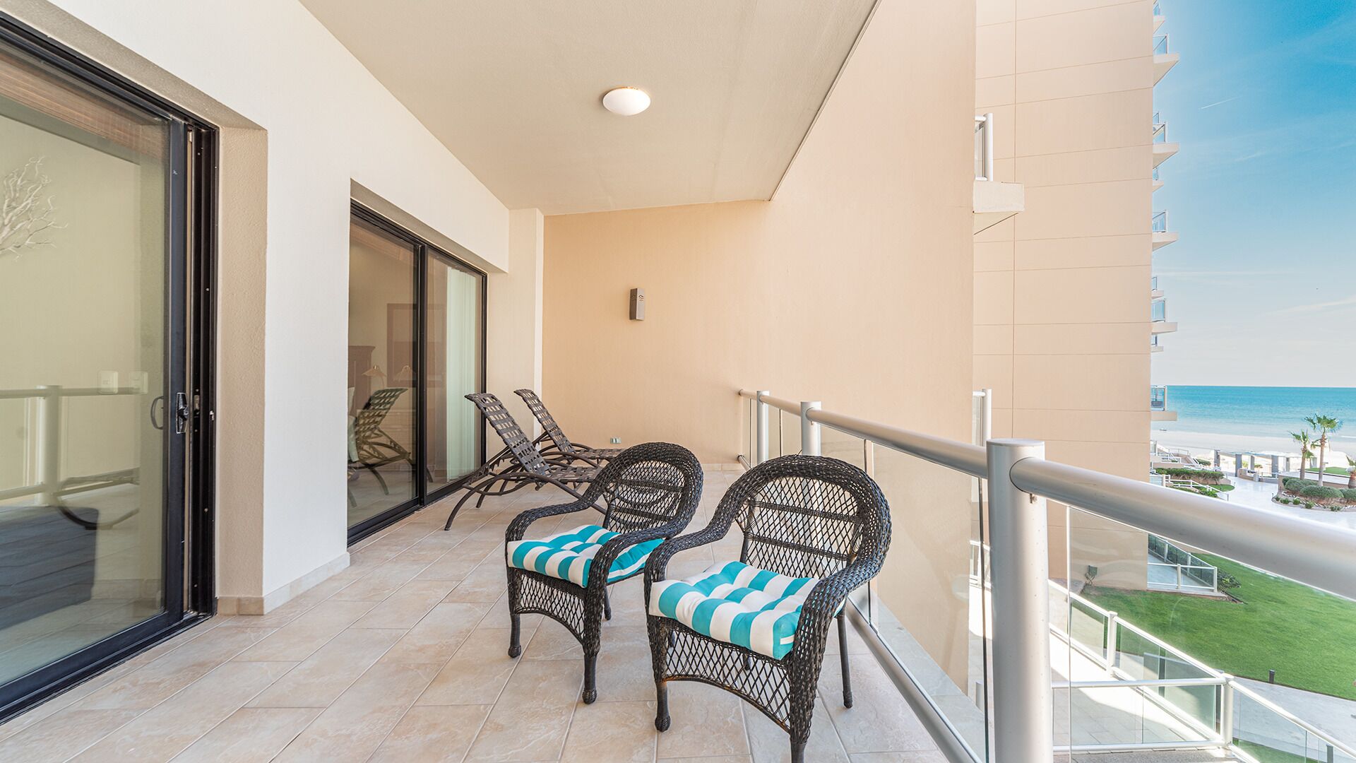 A balcony with wicker chairs, a glass door, and a view of the beach.