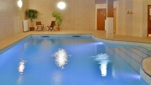 An indoor swimming pool with tiled walls, two potted plants, and two wooden chairs.