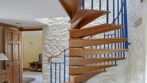A spiral staircase with wooden steps and blue railings in a room with a stone wall and a wooden door.